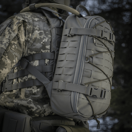 M-Tac Ryggsäck Sturm Elite Gen.II bärs av person i militär utrustning, grå färg, utrustad med MOLLE-system och elastisk snörning.