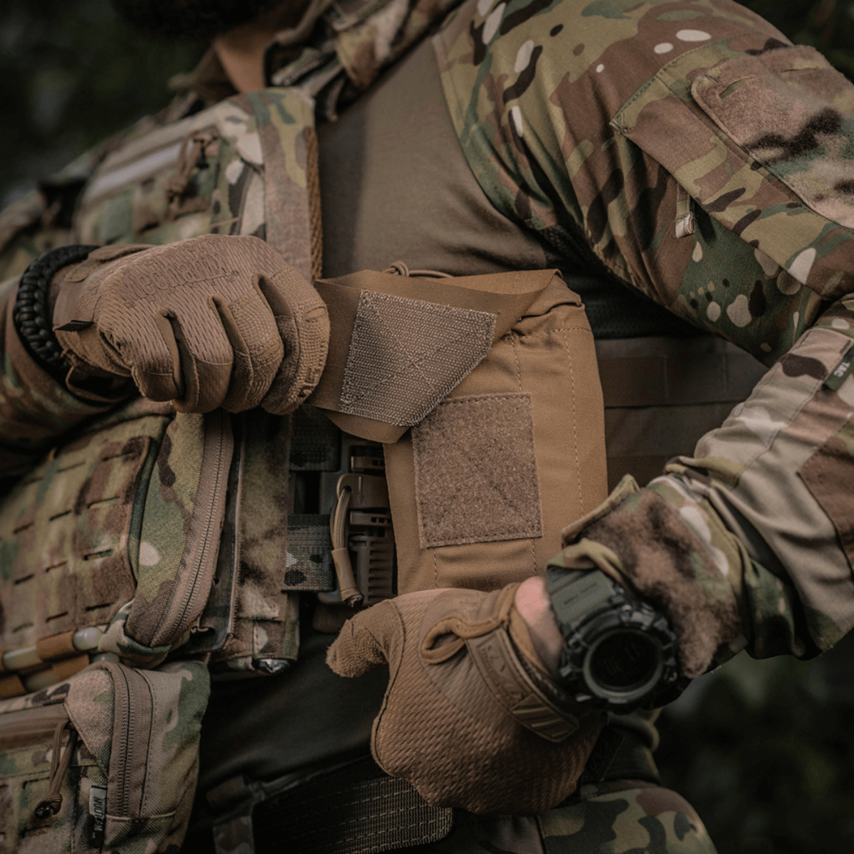 Mand iført taktisk tøj bruger M-Tac Mediclomme Small Vertical Elite til førstehjælpsudstyr, robust og slidstærk.