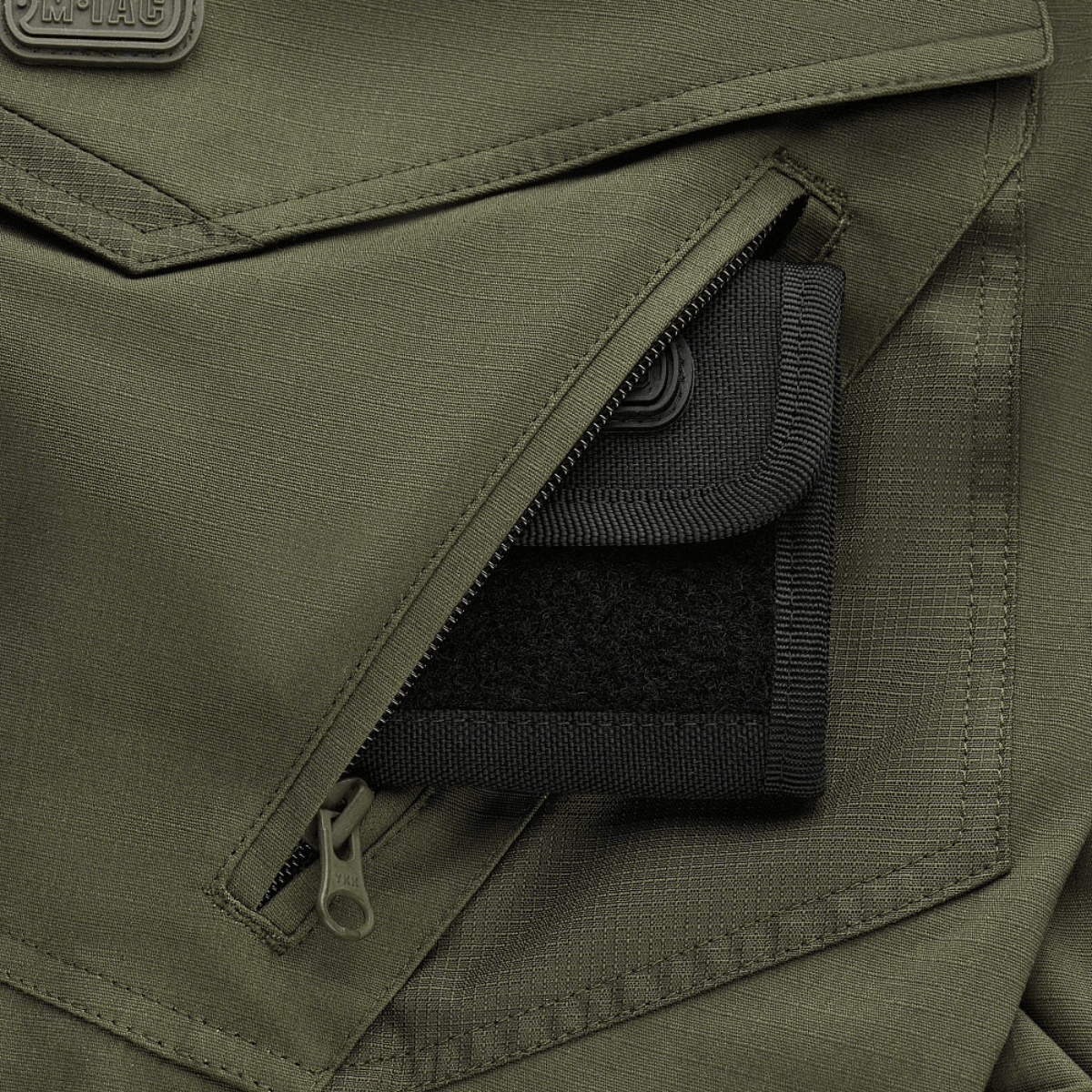 Nærbillede af en lomme på M-Tac Shorts Aggressor Gen.II Flex i olivengrøn rip-stop materiale med lynlåsdetalje.