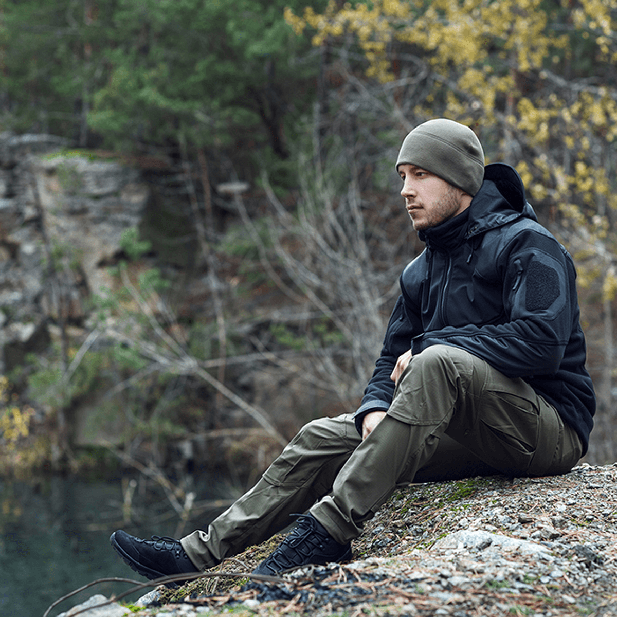 Mand sidder iført M-Tac Norman Windblock Fleecejakke ved en skovsø om efteråret, designet til komfort og varme.