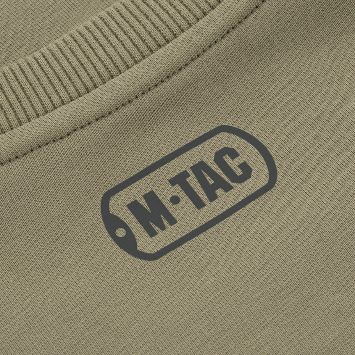 Nærbillede af M-Tac Pullover 4 Seasons logo på beige stof med ribbet kant.
