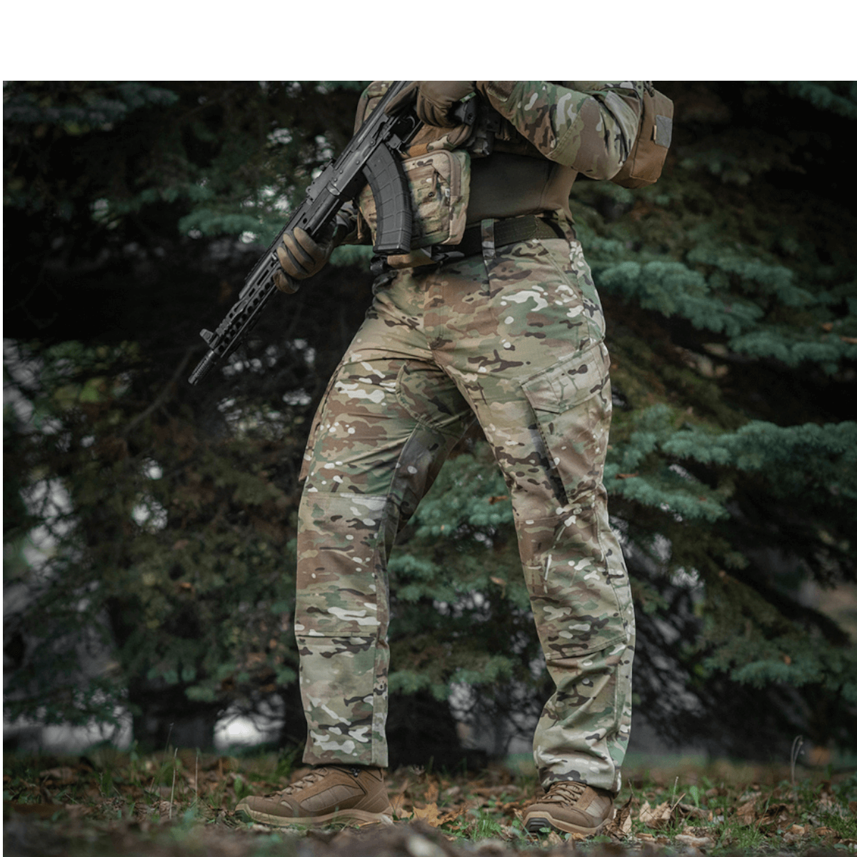 Mand iført M-Tac Feltbukser NYCO i kamuflage i en skov, holdbar og åndbar feltbeklædning til outdoor aktiviteter.