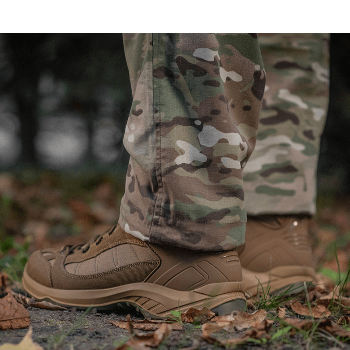 M-Tac Feltbukser NYCO fremviser robust camouflagedesign med holdbare fittings, ideelle til feltbrug, set i skovmiljø.