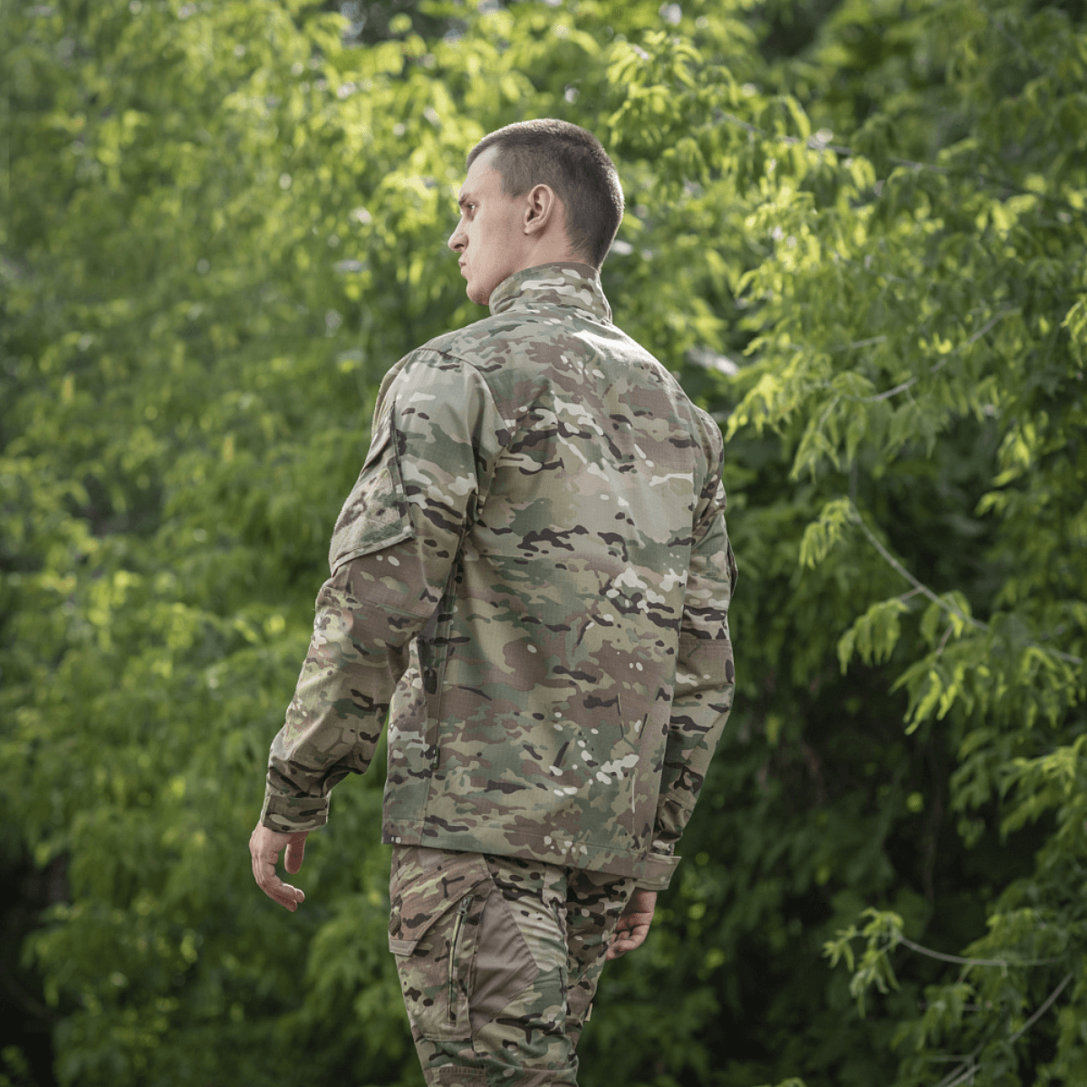 Mand iført M-Tac Feltjakke NYCO med Multicam-mønster, lavet af slidstærkt amerikansk NYCO-stof, i skovomgivelser.