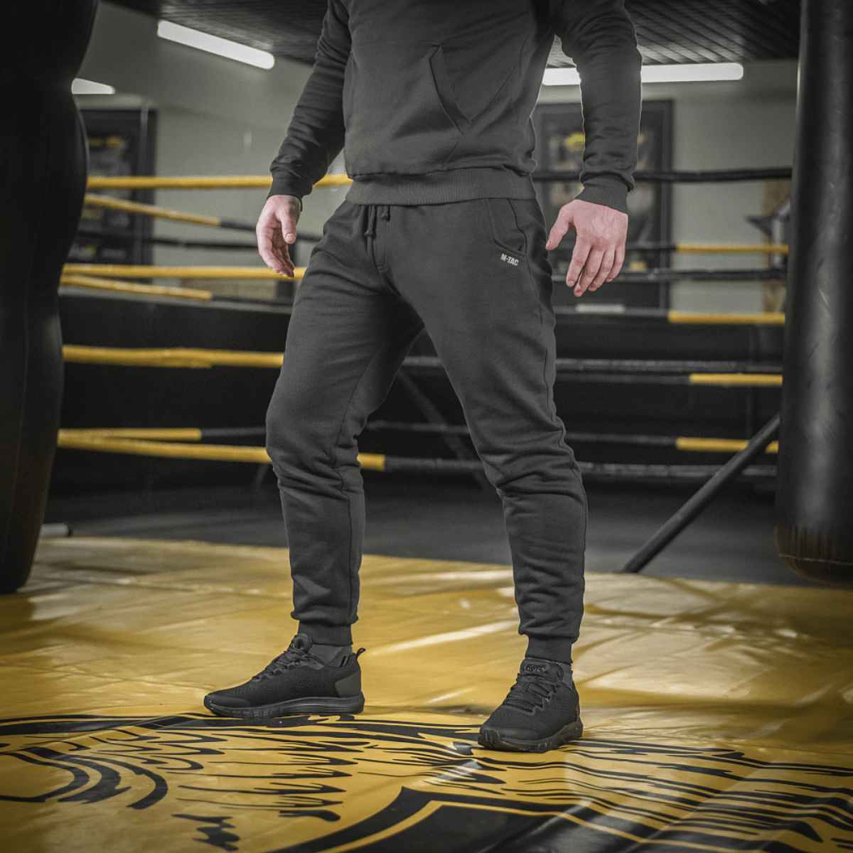 Mand iført M-Tac Bukser Cotton Classic i træningscenter, fremhæver alsidige sportbukser med komfort og stil.
