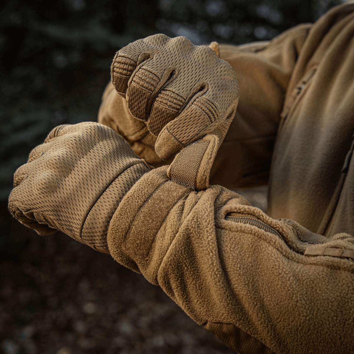 Person iført M-Tac Division Gen.II Windblock Fleecejakke justerer ærme i skovmiljø for optimal varme og vindbeskyttelse.