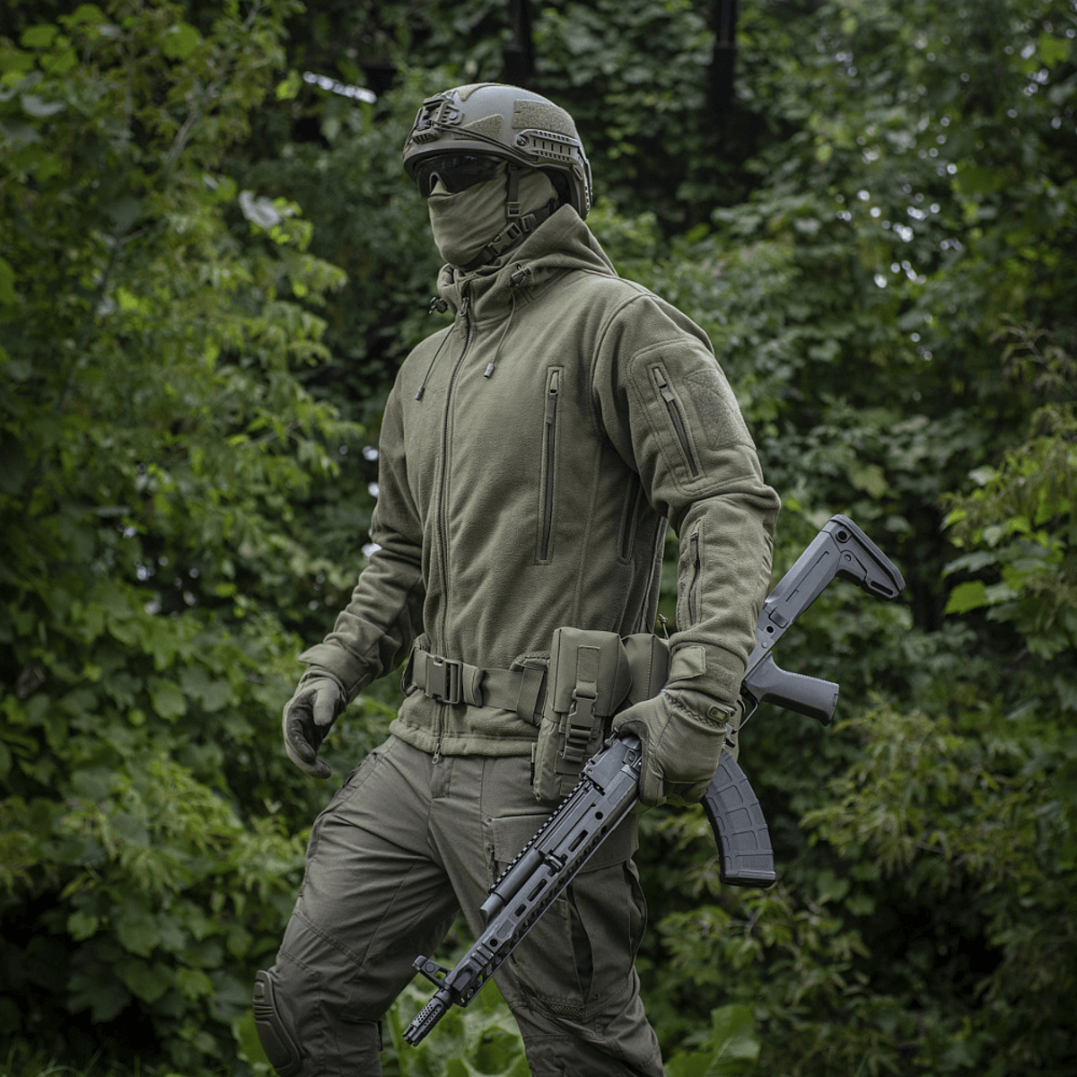 Person iført M-Tac Division Gen.II Windblock Fleecejakke, designet til maksimal varme og vindbeskyttelse, vandrer i skovområde.