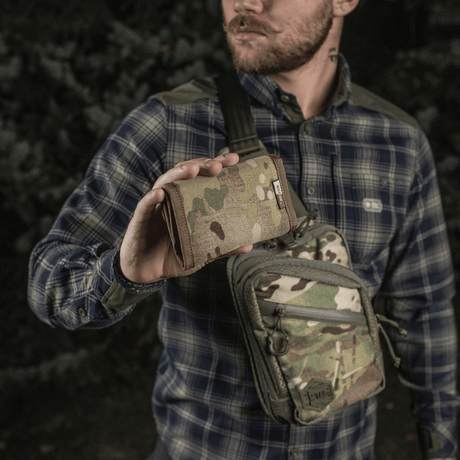 Man håller M-Tac Plånbok Elite Gen.II i kamouflagemönster, gjord i Cordura 500D med YKK-dragkedjor, i skogsmiljö.