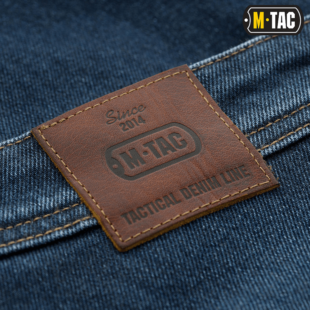 Brun M-Tac Jeans Tactical Gen. I Cordura Regular Fit læder mærkat på denim stof, fremhæver slidstærk Cordura stofkvalitet.