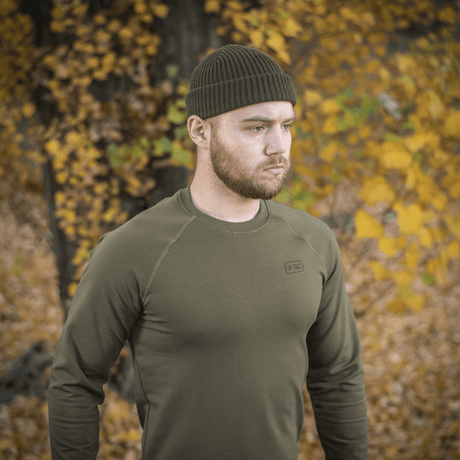 Man bär M-Tac Raglan Athlete sweatshirt i oliv i höstlandskap, framhäver raglanärmarnas flexibilitet och minimalistiska design.