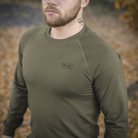 M-Tac Raglan Athlete i olivgrön med raglanärmar, perfekt för dagligt bruk och sport, ses i utomhusmiljö bland höstlöv.