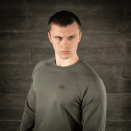Man i M-Tac Raglan Athlete sweatshirt i olivfärg, visar mångsidighet och minimalistisk design med raglanärmar för rörelsefrihet.