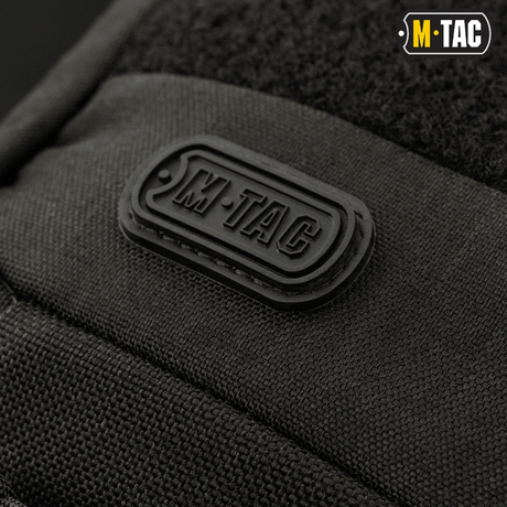 Närbild av M-Tac-logotypen på M-Tac Buckler Taske Elite, en svart taktisk väska med MOLLE-system och dolt vapenfack.