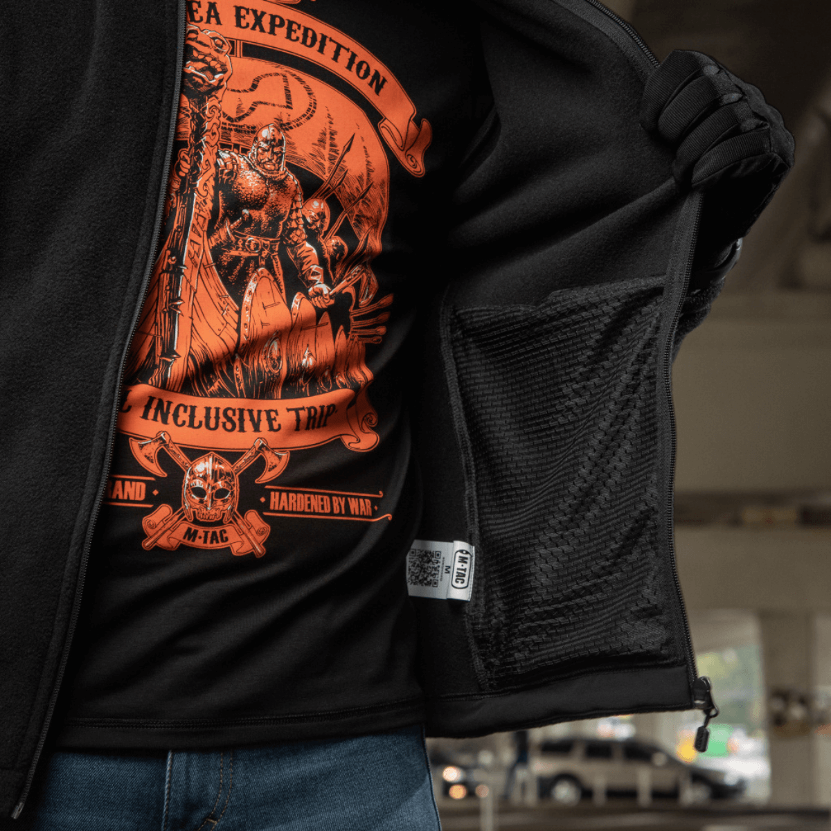 Person iført M-Tac Nord Polartec Fleecejakke viser inderfor og grafisk tryk.