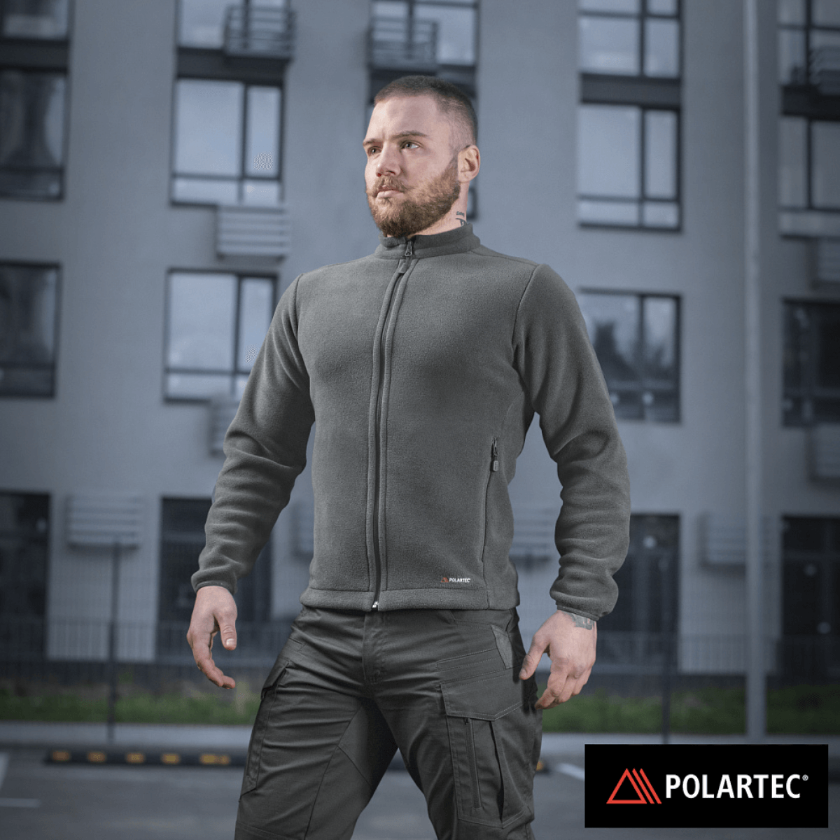 Mand iført M-Tac Nord Polartec Fleecejakke, designet til stil og varme, med Polartec® 200 Series fleece mod en baggrund af et lejlighedskompleks.
