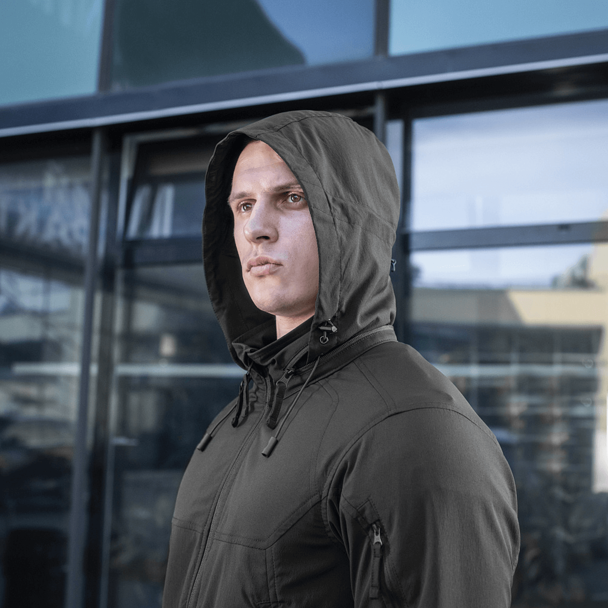 Mand iført M-Tac Flash Jakke, ideel til sport og vandreture, viser jakken med hætte i urbant miljø.