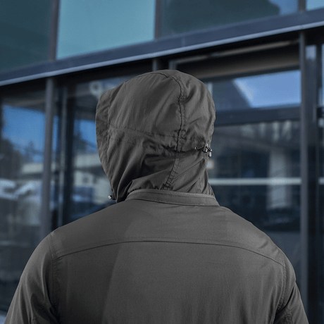 Person iført en M-Tac Flash Jakke set bagfra mod en moderne glasfacade, fremhæver jakkens praktiske og enkle design uden velcrofelter.