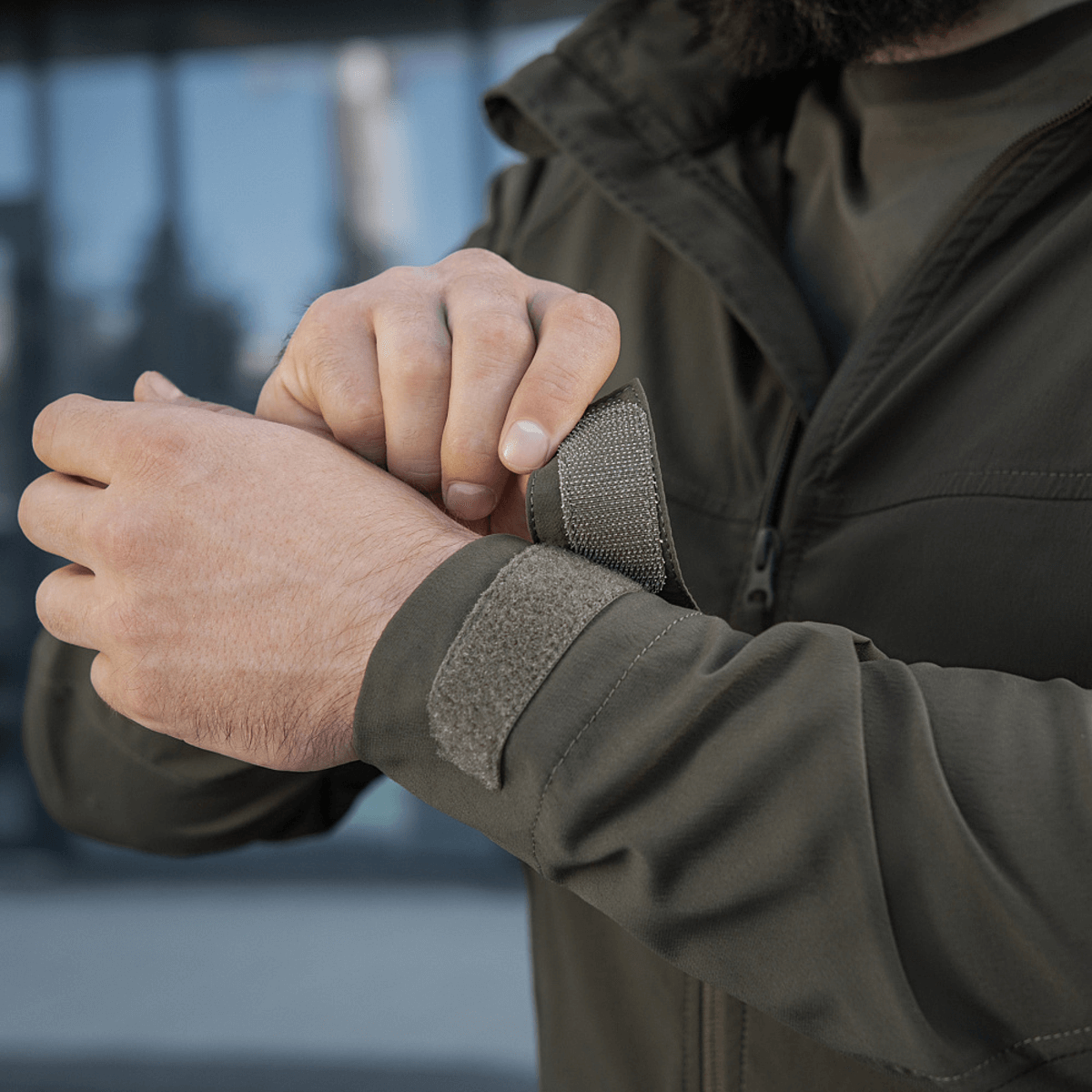 Mand iført M-Tac Flash Jakke justerer ærmet i en urban setting. Letvægtsdesign ideelt til vandreture og aktiv hverdag.