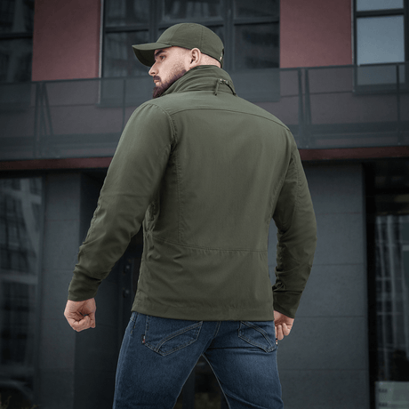 Mand iført M-Tac Flash Jakke foran moderne bygning. Let og alsidig jakke ideel til hverdag og aktiviteter. Ingen velcro på ærmerne.