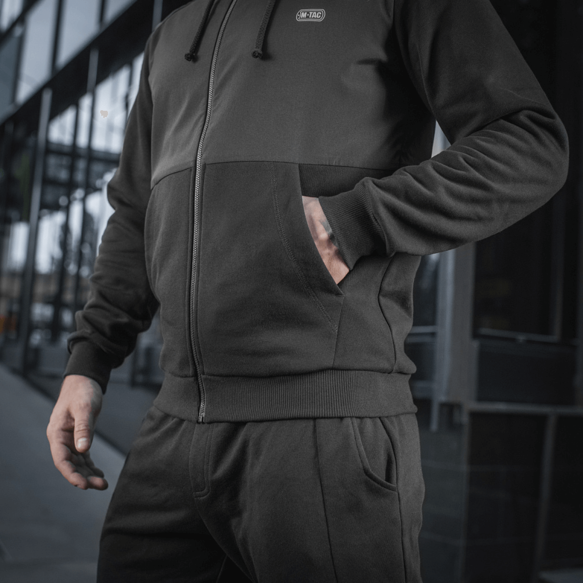 Sort M-Tac Pilgrim Bomberjakke med hætte og ribbede manchetter, ideel til daglig brug og sport. Holdbar kvalitet med central lynlås.