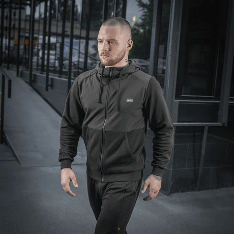 Mand iført sort M-Tac Pilgrim Bomberjakke går på gaden, fremhæver stilfuld og praktisk design, ideel til hverdagsbrug.