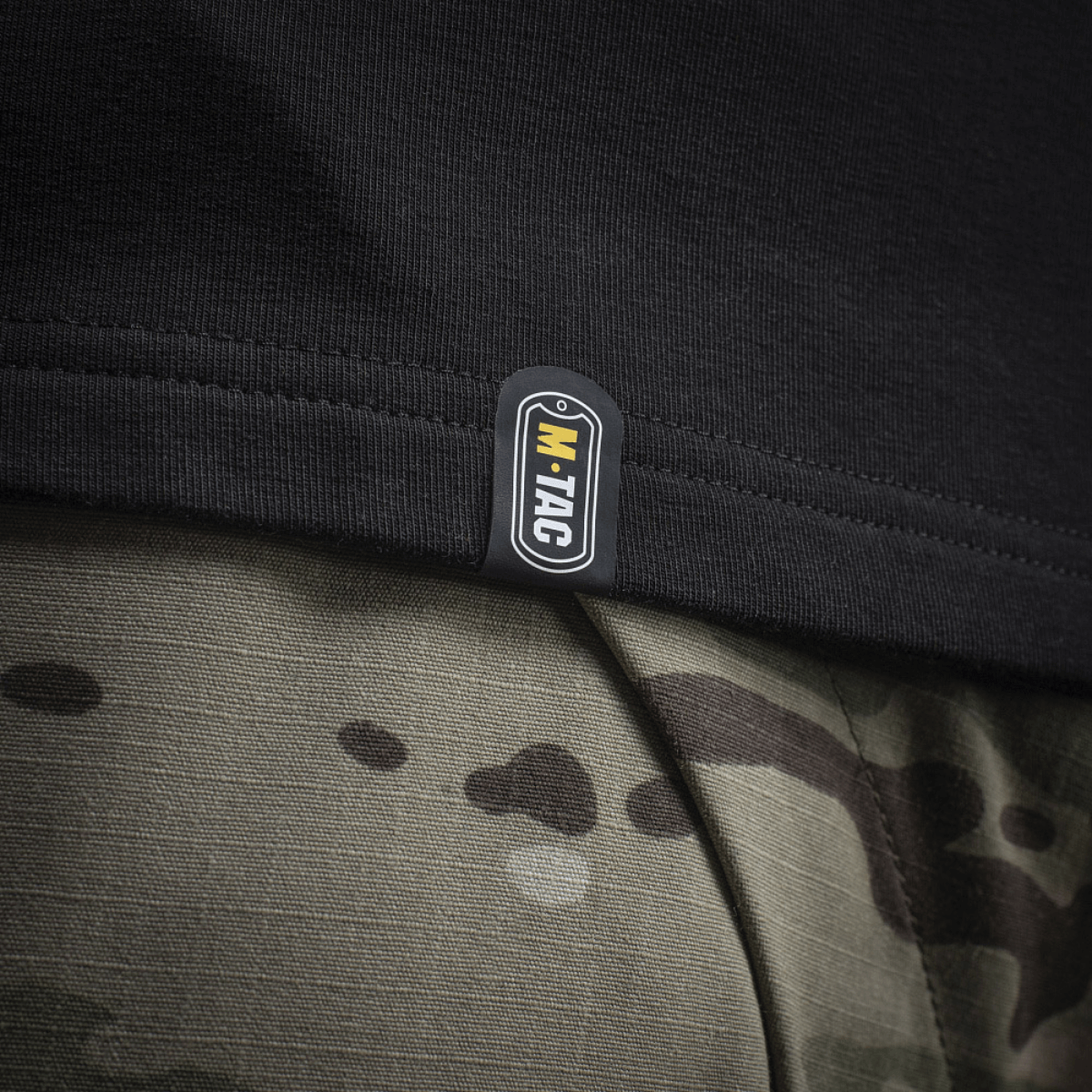 Detalje af M-Tac Raglan Odin Mystery med tydeligt M-Tac logo, sort kant på sejlrib, kombineret med camouflageprint bukser.
