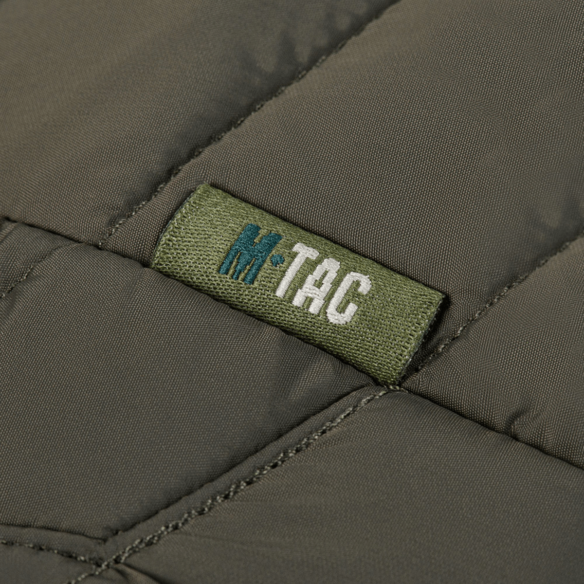 Detalje af M-Tac Damevest Primaloft med slidstærkt vandafvisende yderstof. Fokus på M-Tac logoet og den tekniske kvalitet.