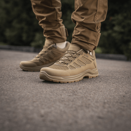 M-Tac Tactical Sneakers IVA på personens fødder, ideelle til sommeraktiviteter og trekking, vises på asfalt mod en grøn baggrund.