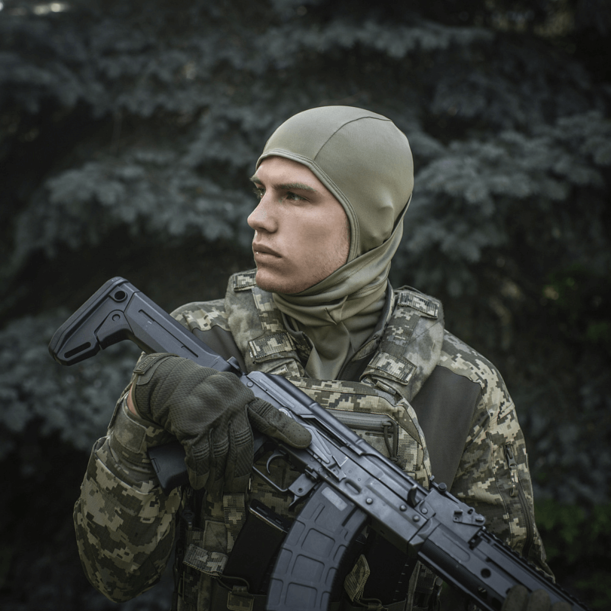 Soldat iført M-Tac Sweater-Ninja-Balaclava Premium i skovklædning, holder våben, optimal til fugthåndtering og komfort.