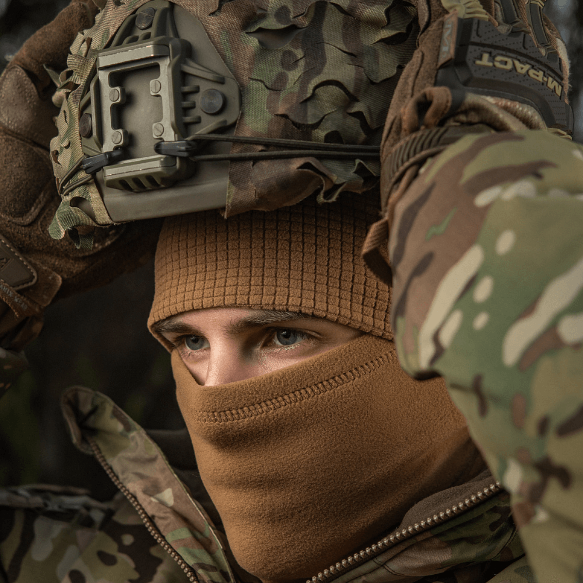 Mand iført M-Tac Rip-Stop Fleece Hjelmliner under camouflagehjelm, egnet til koldt vejr og udendørs aktiviteter.