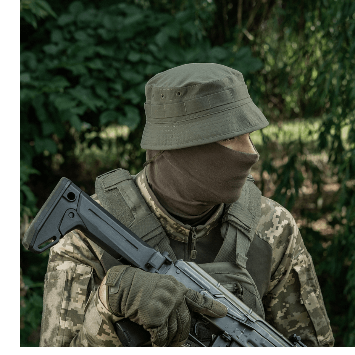 Soldat i camouflagetøj med M-Tac Panamahat Gen. II Summer Flex, holder riffel, omgivet af skov. Perfekt til sommerture og solbeskyttelse.