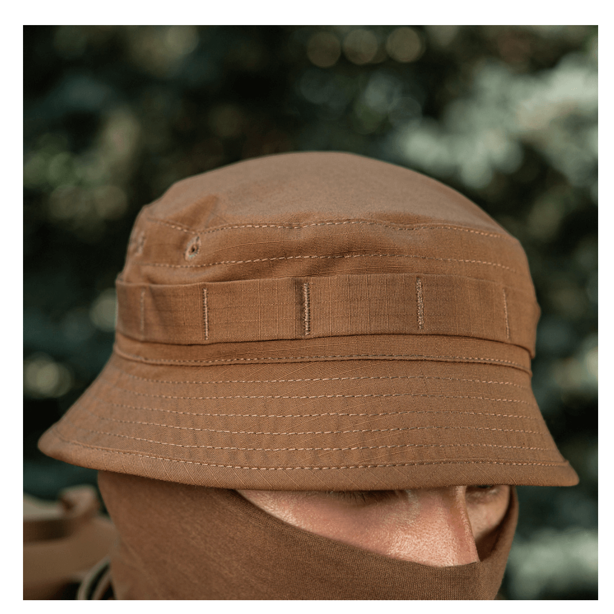 M-Tac Panamahat Gen. II Flex Rip-Stop i brun rip-stop stof, designet til hverdagsbrug, vises tæt på en persons hoved i naturen.