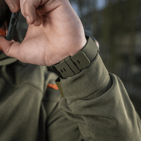 Person som bär M‑Tac Multifunktionellt Taktiskt ur med robust urkass och rem, idealiskt för friluftsliv och militärt bruk