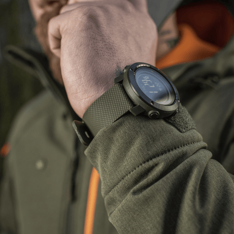 M‑Tac Multifunktionellt Taktiskt ur på mannens handled i utomhusmiljö, idealiskt för friluftsliv med avancerade funktioner och robusthet