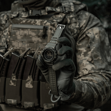 M-Tac Tactical Klocka med Kompass 2233 hålls av person i taktisk klädsel, visar robust urdesign lämpad för friluft och vardaglig användning.