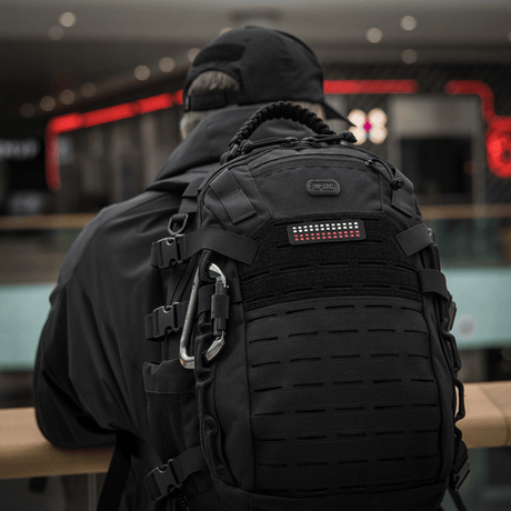 En person med ryggsäck bär M-Tac Patch Flag 25x80 Mini Squares i slitstark Cordura 500D med velcrofäste, lämplig för taktisk utrustning.