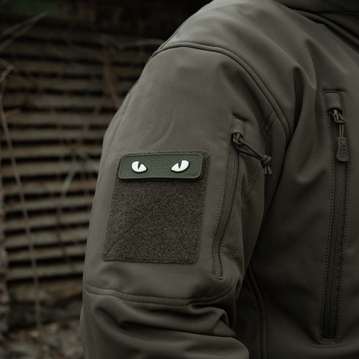 M-Tac Cat Eyes 3D PVC Patch på jakkeærme i taktisk miljø, viser lysreflekterende og fluorescerende design, fastgjort med Velcro.