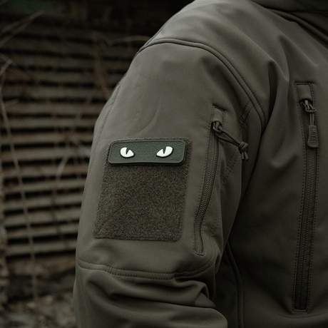 M-Tac Cat Eyes 3D PVC-patch på jackärm i taktisk miljö, visar ljusreflekterande och fluorescerande design, fäst med Velcro.