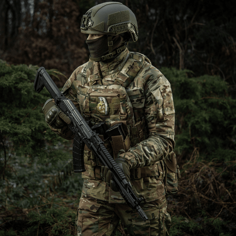 En soldat i kamouflage med en M-Tac Patch M67 granat 3D PVC på sin väst, utrustad med taktisk gear i en skogsmiljö.