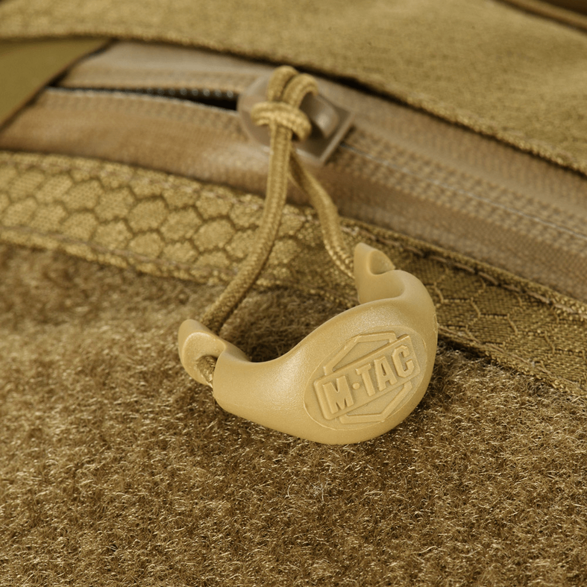 Detalje af M-Tac Sling Pistol Taske Elite Hex med Velcro, viser lynlås og håndtag med logo, lavet af slidstærk Cordura-materiale.