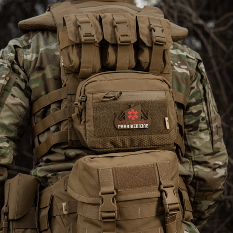 Taktisk ryggsäck med 'Paramedicine'-patch i kamouflagemönster sedd bakifrån i naturen, robust och hållbar för utomhusbruk.
