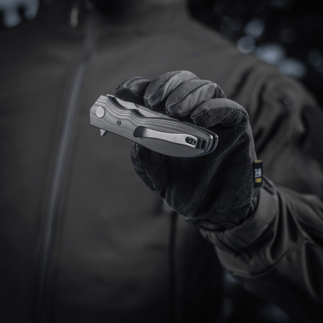 Person håller M-Tac Outdoor & Militär fällkniv - Type 6 med svart G10-komposithandtag i handske.