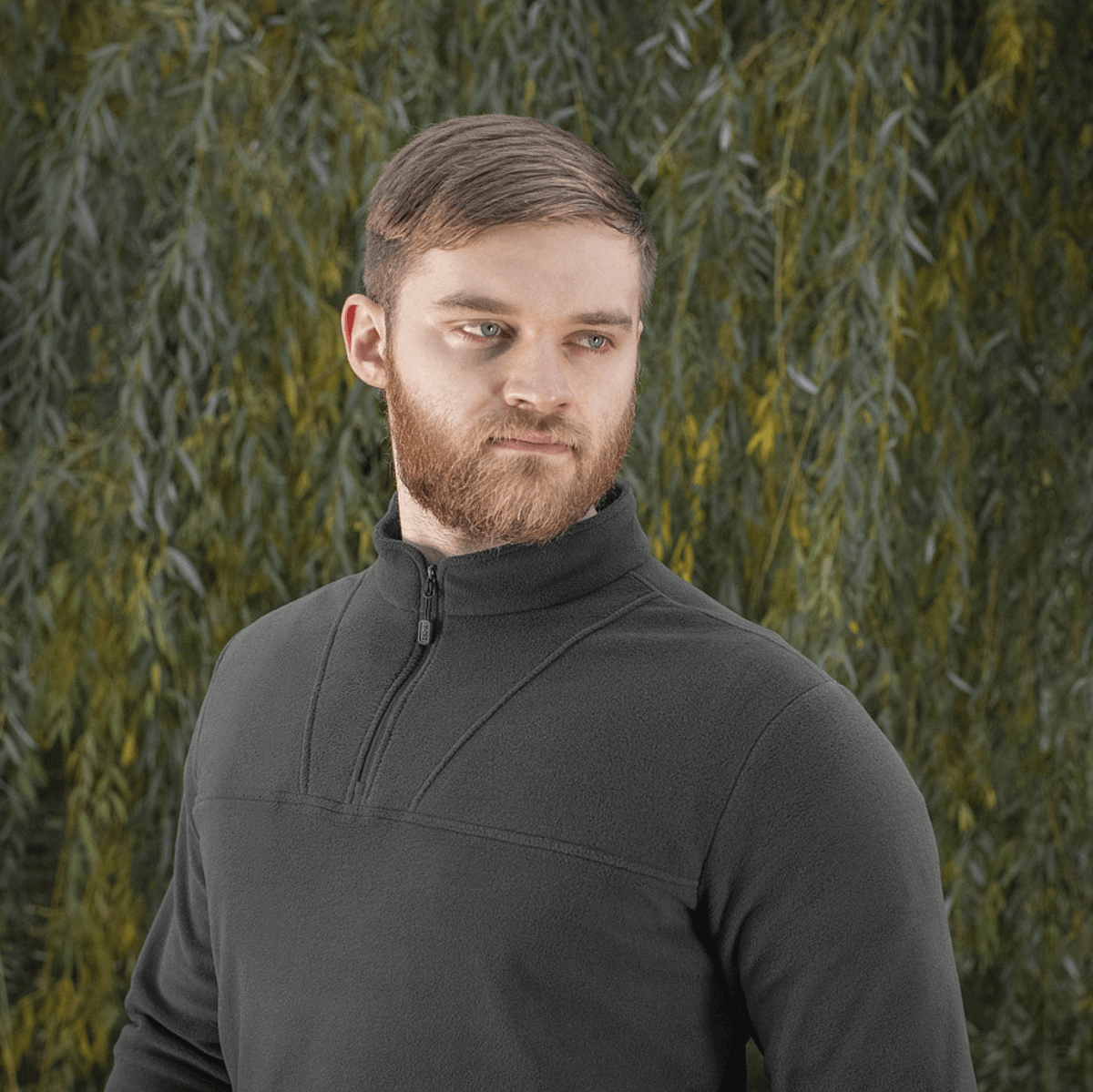 Mand iført M-Tac Delta Polartec Fleecejakke i sort, med halv lynlås, foran en naturlig grøn baggrund. Stilren og funktionel design.