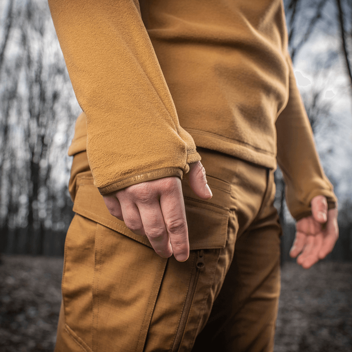 M-Tac Delta Polartec Fleecejakke i skoven, viser fleece-ærme og praktisk design, perfekt til kolde dage i naturen.