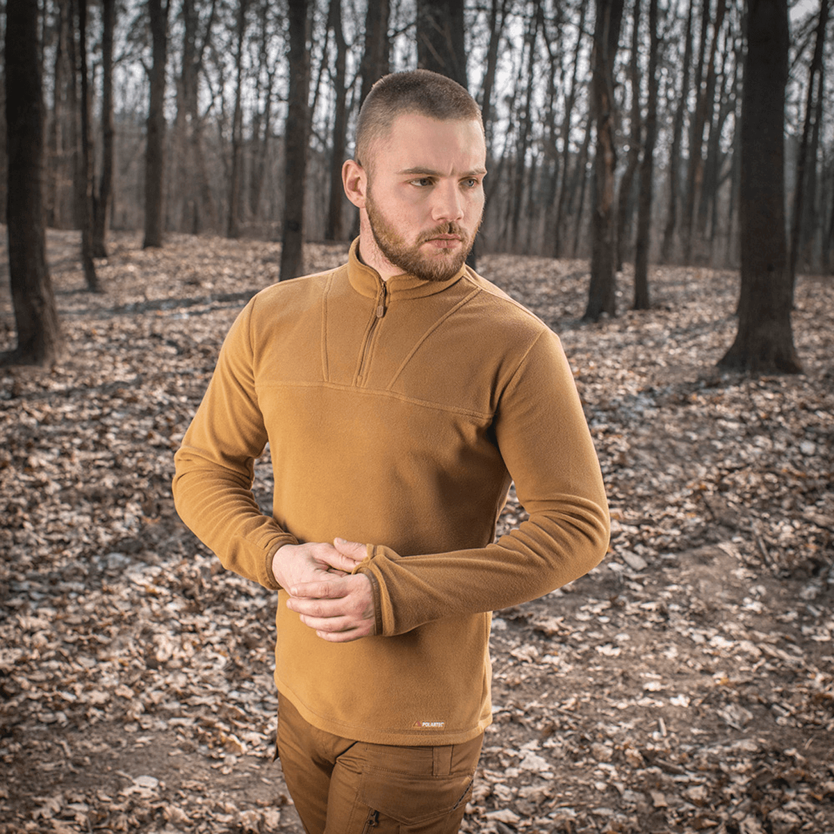 Mand iført M-Tac Delta Polartec Fleecejakke i skoven på en kold dag, viser fleecejakken med halv lynlås og varmeisolerende egenskaber.