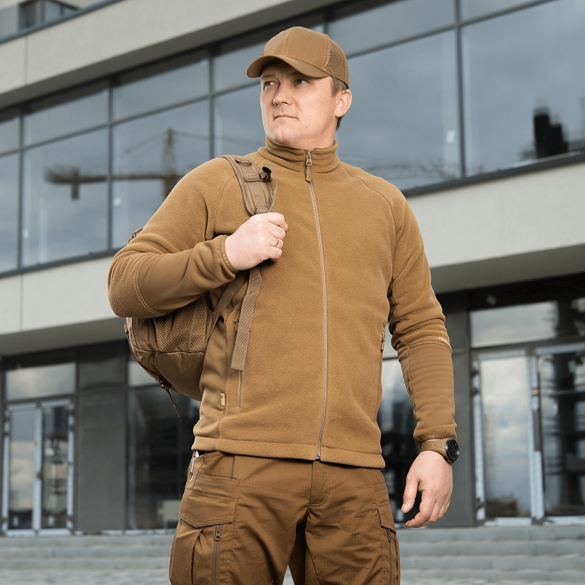 Mand iført M-Tac Polartec Sport Fleecejakke foran en moderne bygning, understreger stil og praktisk funktionalitet.