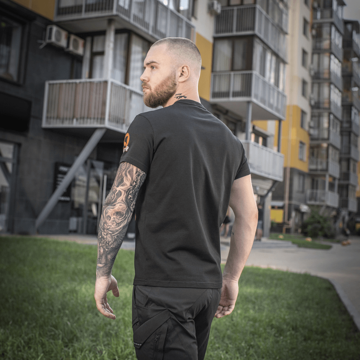 Mand bærer en M-Tac T-shirt Black Sea Expedition foran moderne bygninger