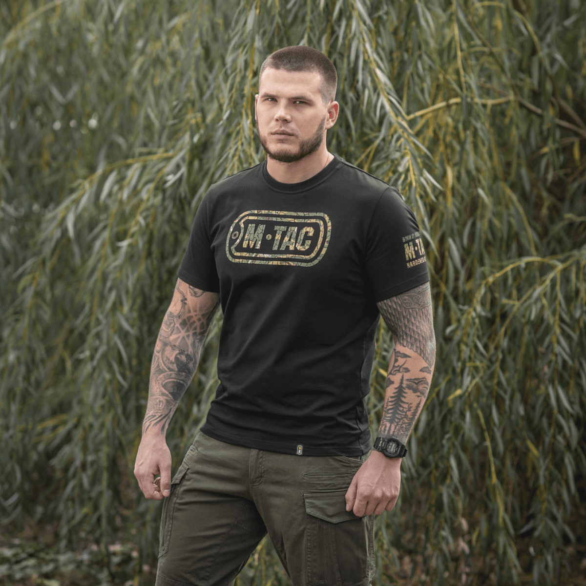 Mand iført M-Tac T-Shirt Logo med camouflage og slogans i naturen