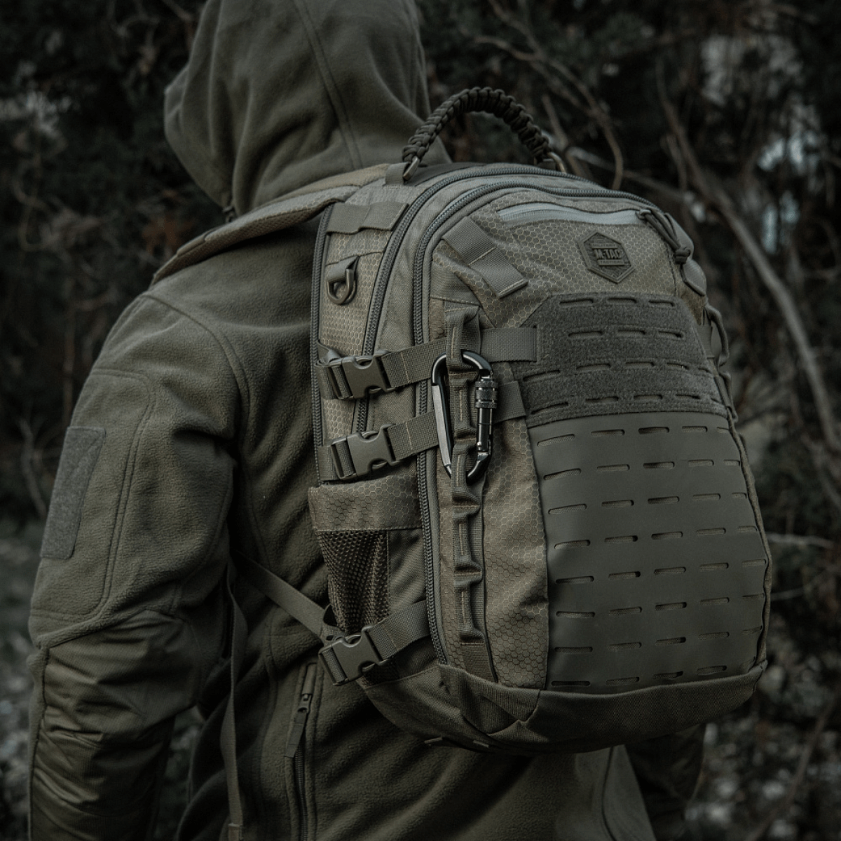 Rygsæk med M-Tac Karabinhage 10 cm i militært udstyr, fremstillet af 40Cr legeret stål, vist i udendørs skovmiljø.