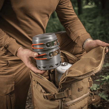 Person packar M-Tac Individuellt kokset för brännare i ryggsäck i skogen, idealiskt för friluftsliv och camping, tillverkat i anodiserad aluminium.